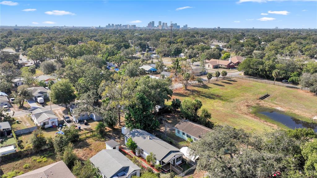 An aerial view shows a residential neighborhood with houses, trees, and a distant city skyline — 3203 E 38TH AVENUE, TAMPA, FL