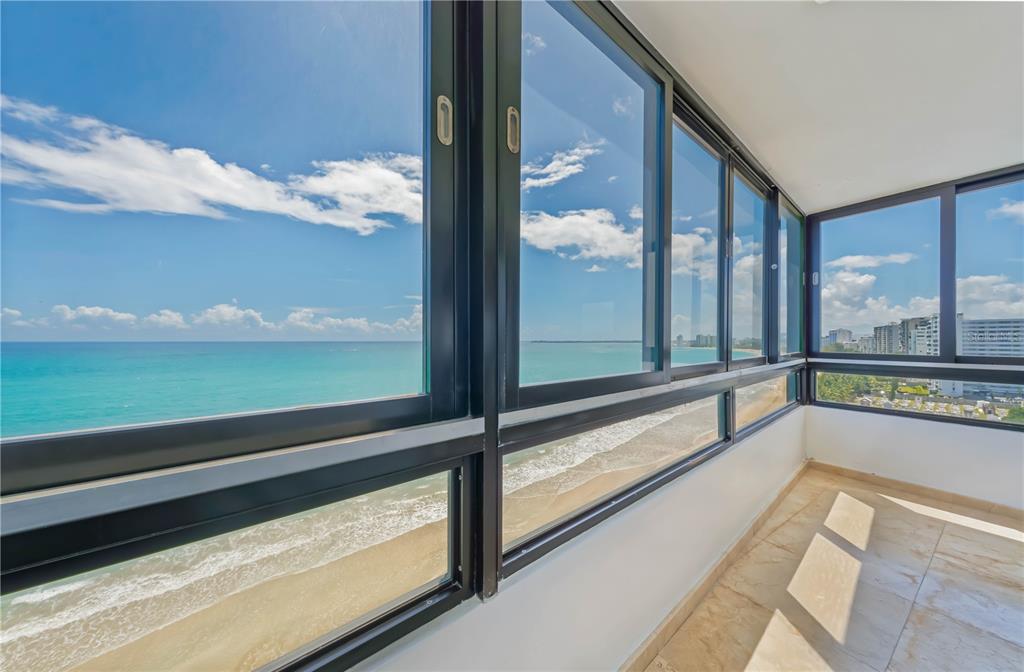 A sunroom with tile flooring and large windows overlooking the ocean and a sandy beach — 4123 ISLA VERDE AVENUE UNIT 1106, CAROLINA, PR