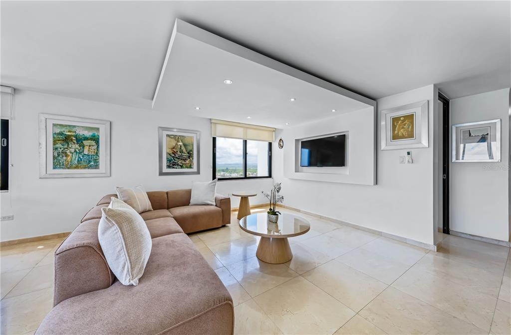 A modern living room features a tan sectional sofa, a glass coffee table, and recessed lighting — 4123 ISLA VERDE AVENUE UNIT 1106, CAROLINA, PR