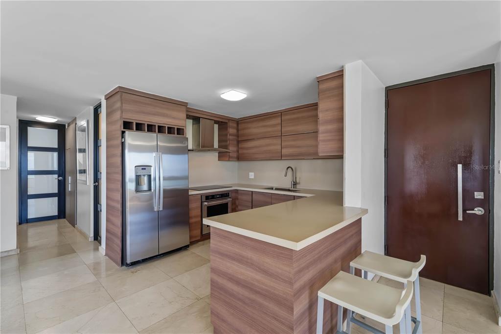 A modern kitchen features wood-grain cabinetry, stainless steel appliances, and a breakfast bar — 4123 ISLA VERDE AVENUE UNIT 1106, CAROLINA, PR
