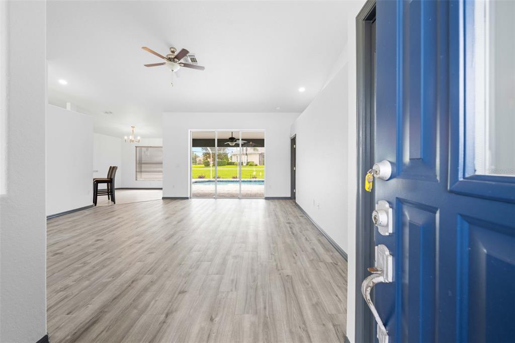 An open-concept living area with light wood-look flooring leads to a sliding glass door — 14074 ANDREW SCOTT ROAD, SPRING HILL, FL