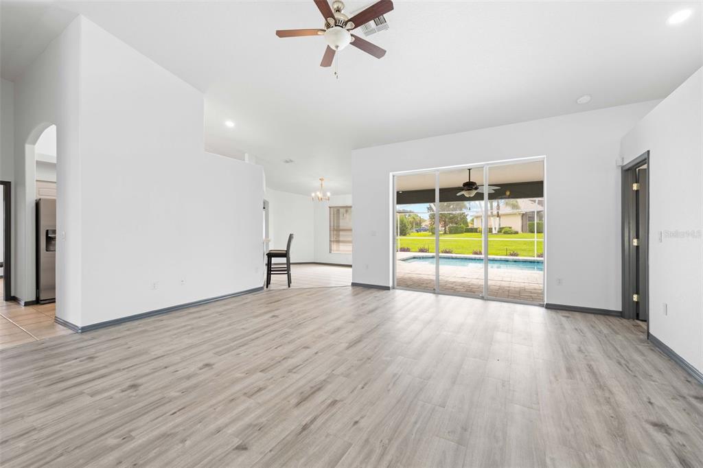A spacious living area with light wood-look flooring, white walls, and sliding glass doors to a pool — 14074 ANDREW SCOTT ROAD, SPRING HILL, FL