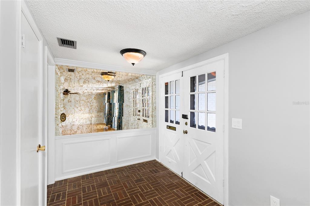 An entryway features a brick floor, white wainscoting, a mirrored wall, and double glass-paneled doors — 3803 SAIL DRIVE, NEW PORT RICHEY, FL