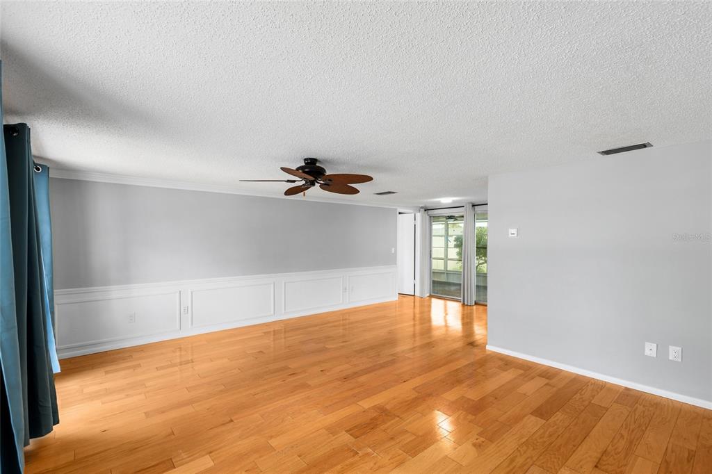 A spacious living room features hardwood floors, white wainscoting, a ceiling fan, and sliding glass doors — 3803 SAIL DRIVE, NEW PORT RICHEY, FL