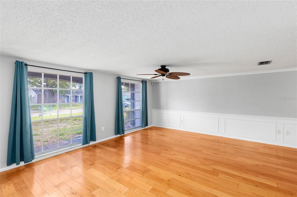 An empty living room features light gray walls, white wainscoting, hardwood floors, and two windows — 3803 SAIL DRIVE, NEW PORT RICHEY, FL