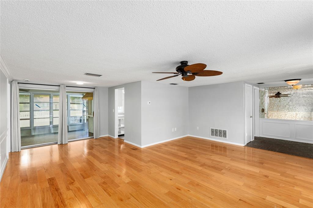 An empty living room with light hardwood floors, a ceiling fan, and sliding glass doors — 3803 SAIL DRIVE, NEW PORT RICHEY, FL