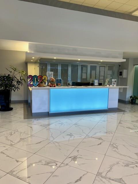 A modern reception area features a glowing blue desk and white marble-patterned tile flooring — 531 N Ocean Boulevard # 1808, Pompano Beach FL 33062, POMPANO BEACH, FL