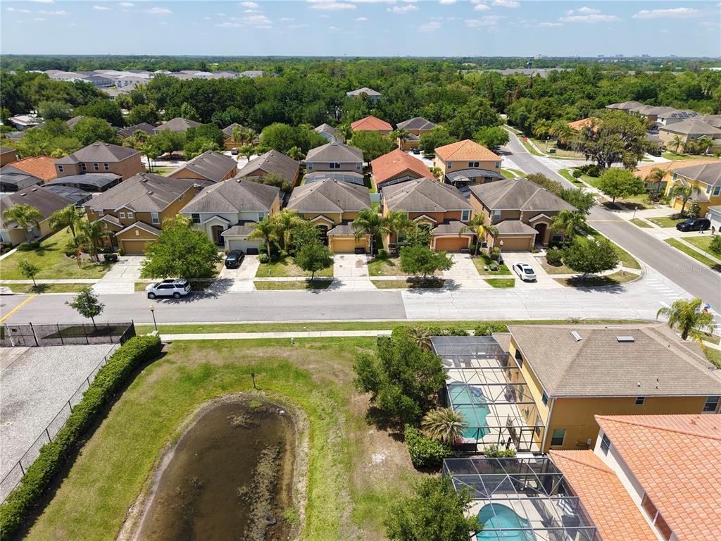 An aerial view shows a suburban neighborhood with houses, swimming pools, and a small pond — 2549 DHARMA CIRCLE, KISSIMMEE, FL