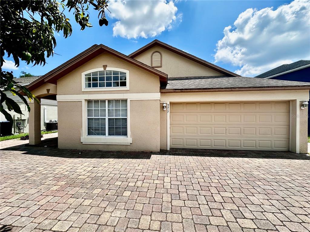 A single-story house with a beige stucco exterior, a two-car garage, and a paver driveway — 9217 TELFER RUN, ORLANDO, FL