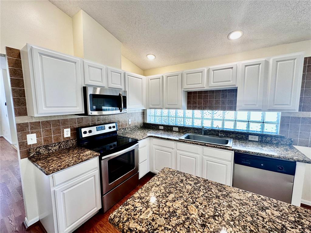 A kitchen with white cabinets, granite countertops, stainless steel appliances, and a glass block backsplash — 9217 TELFER RUN, ORLANDO, FL