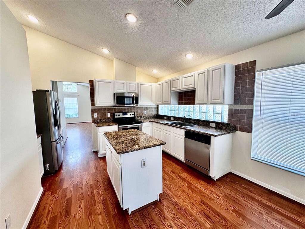 A kitchen features white cabinets, granite countertops, a center island, and a glass block backsplash — 9217 TELFER RUN, ORLANDO, FL