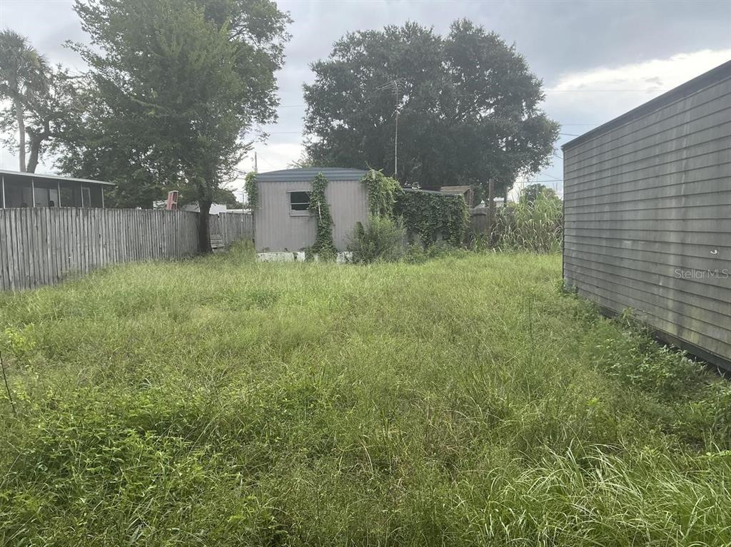 An overgrown grassy backyard features a small, weathered shed and a wooden privacy fence — 4648 NELLIE STREET, EDGEWATER, FL