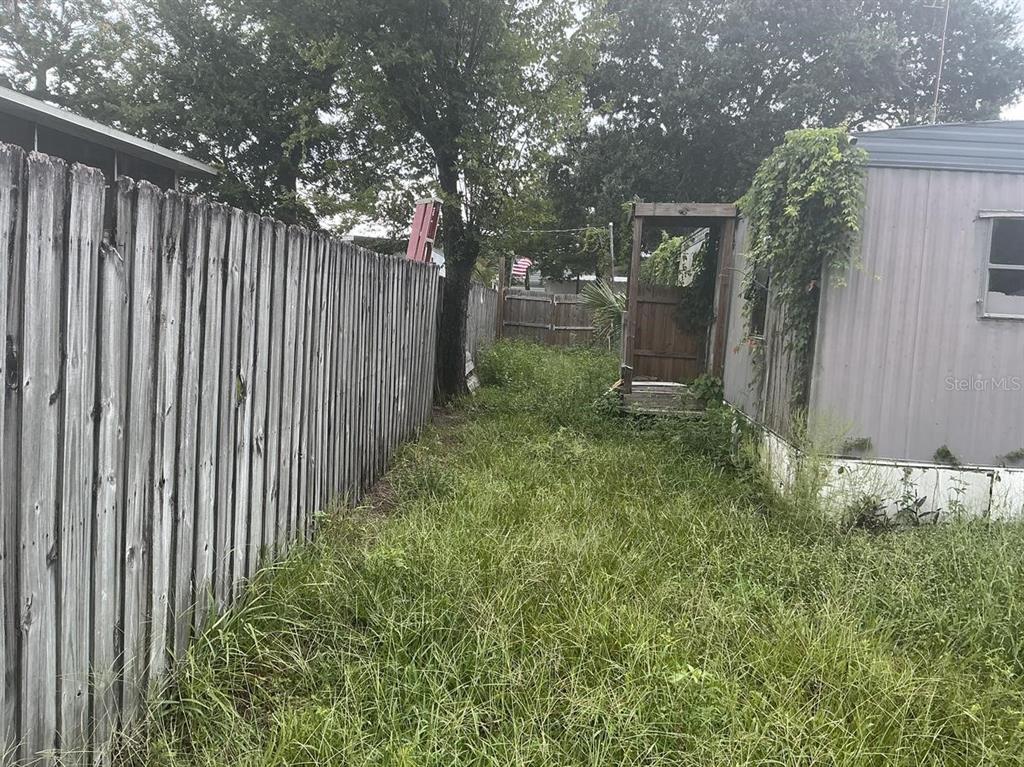 A narrow, overgrown yard sits between a wooden fence and the side of a trailer — 4648 NELLIE STREET, EDGEWATER, FL
