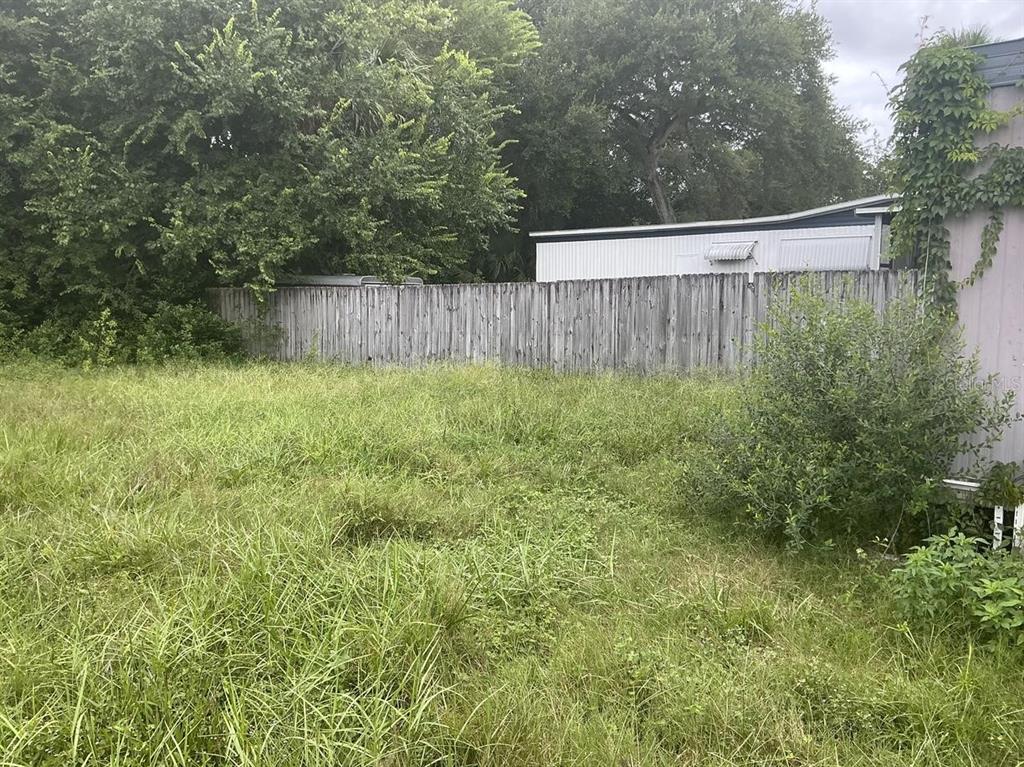 An overgrown grassy yard sits in front of a wooden fence and a mobile home — 4648 NELLIE STREET, EDGEWATER, FL