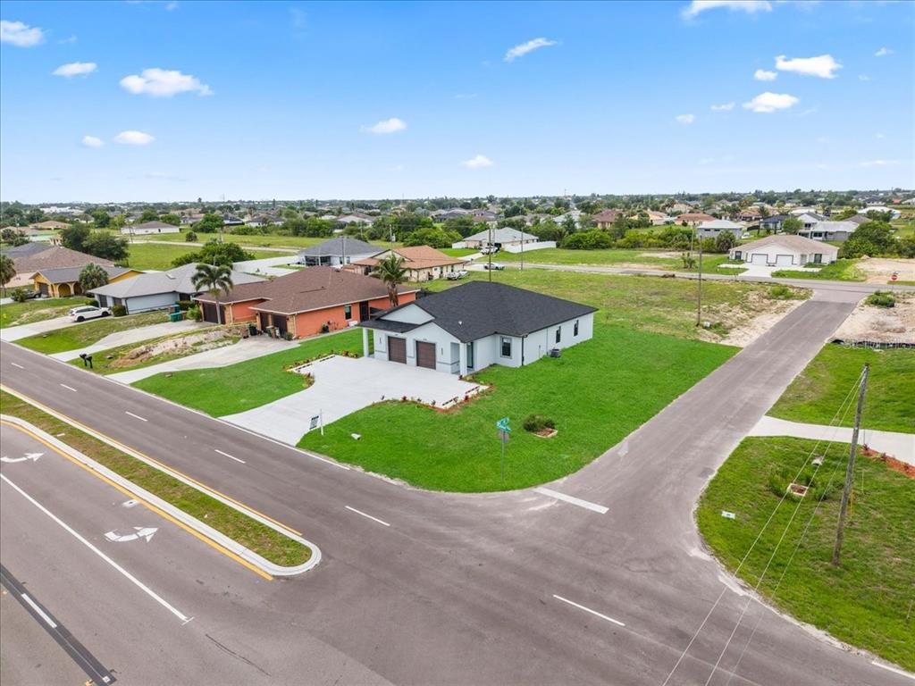 An aerial view shows a modern single-story house with a black roof on a corner lot — 1024/1026 DIPLOMAT PARKWAY E, CAPE CORAL, FL