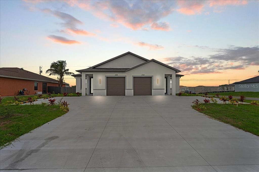 A duplex house with two garage doors and a large concrete driveway at sunset — 1024/1026 DIPLOMAT PARKWAY E, CAPE CORAL, FL