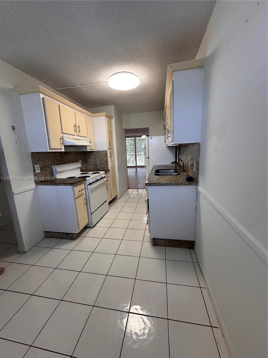A galley kitchen features white cabinets, granite countertops, and white tile flooring — 250 Jacaranda Dr # 305, Plantation FL 33324, PLANTATION, FL