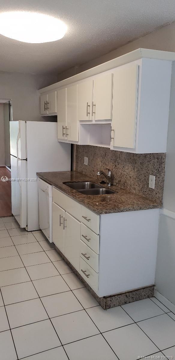 A kitchen features white cabinets, granite countertops, a double sink, and white tile flooring — 250 Jacaranda Dr # 305, Plantation FL 33324, PLANTATION, FL