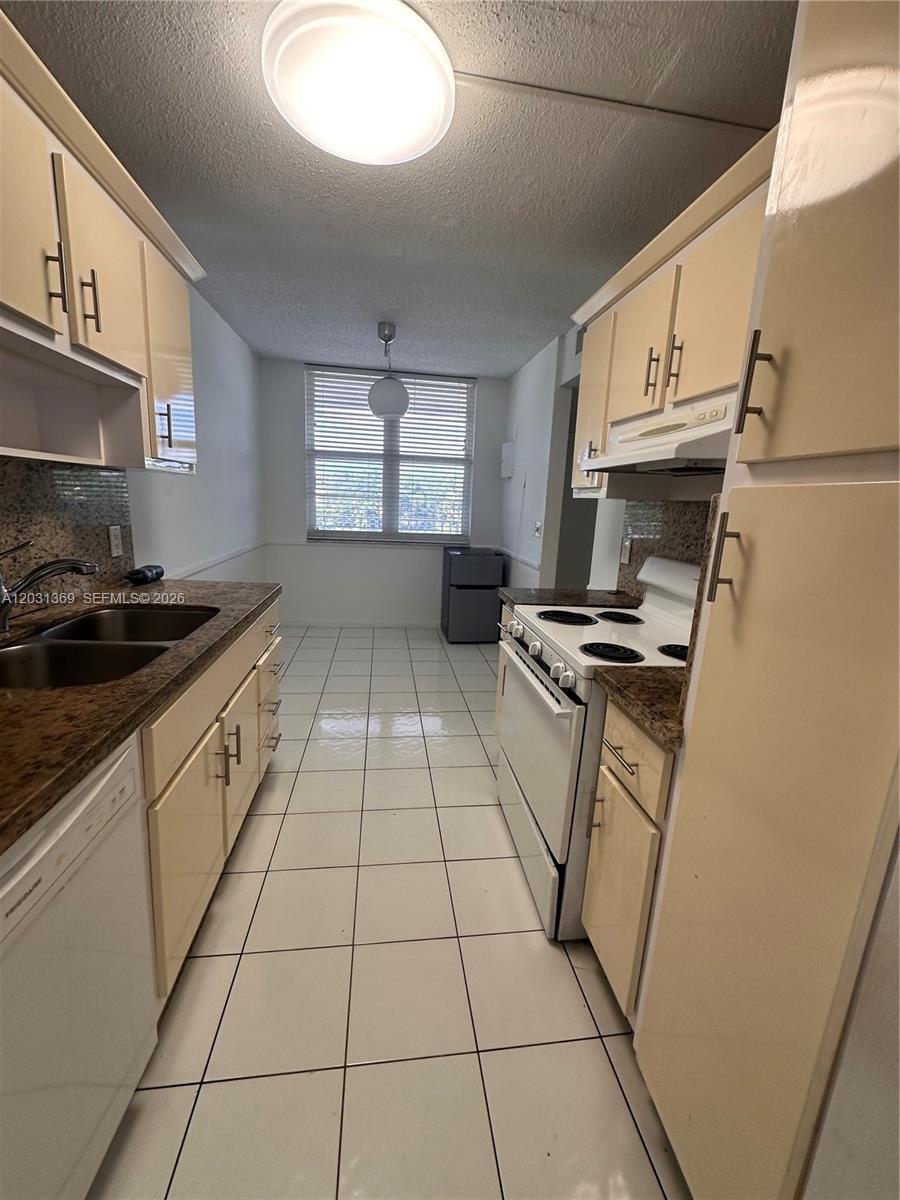 A galley-style kitchen features white tile flooring, light-colored cabinetry, and granite countertops — 250 Jacaranda Dr # 305, Plantation FL 33324, PLANTATION, FL