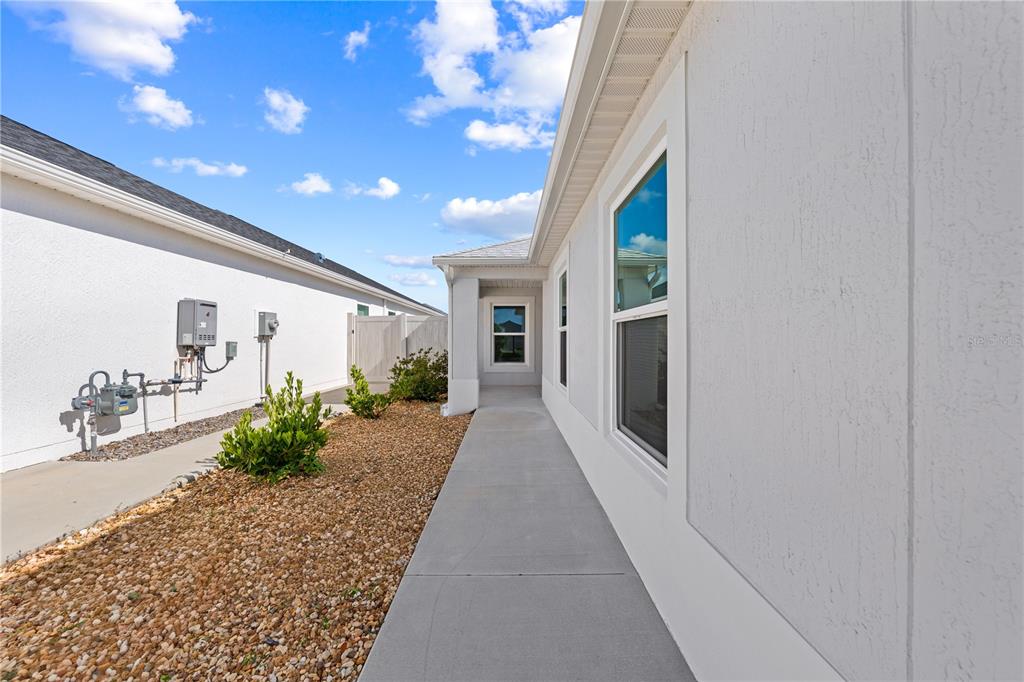 A concrete walkway runs between two white stucco houses with gravel landscaping — 517 LAMINGTON LANE, THE VILLAGES, FL