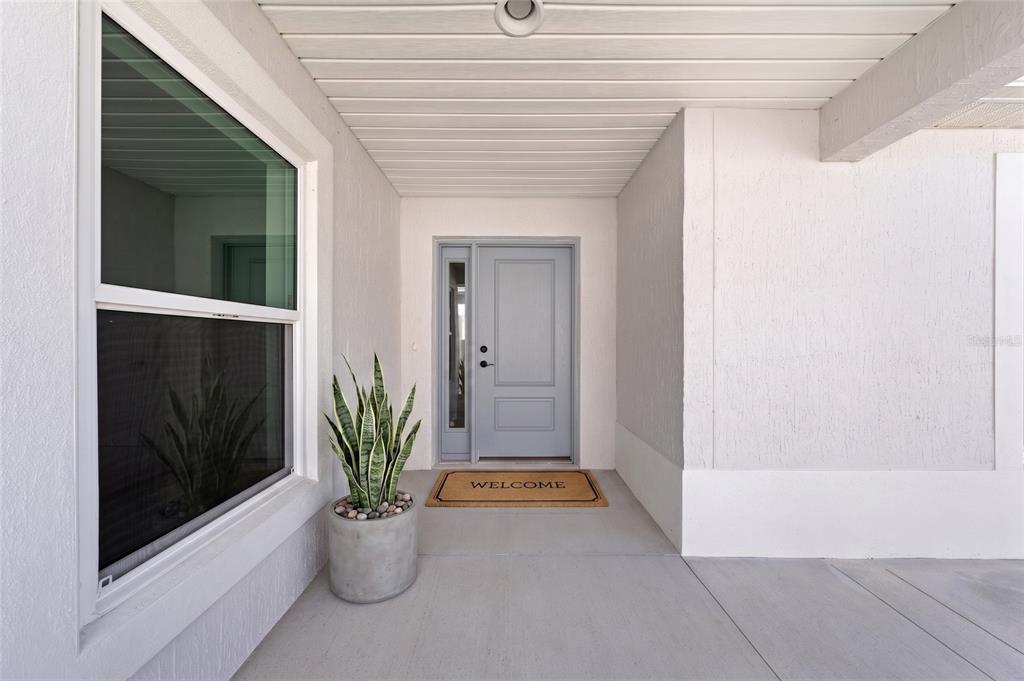 A light-colored front entryway features a gray door, a potted plant, and a welcome mat — 517 LAMINGTON LANE, THE VILLAGES, FL