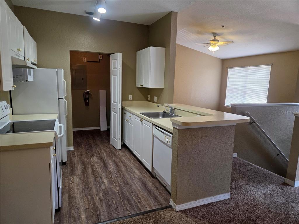 A kitchen with white cabinets, a dishwasher, and a sink overlooks a carpeted living area — 821 GRAND REGENCY POINTE UNIT 203, ALTAMONTE SPRINGS, FL