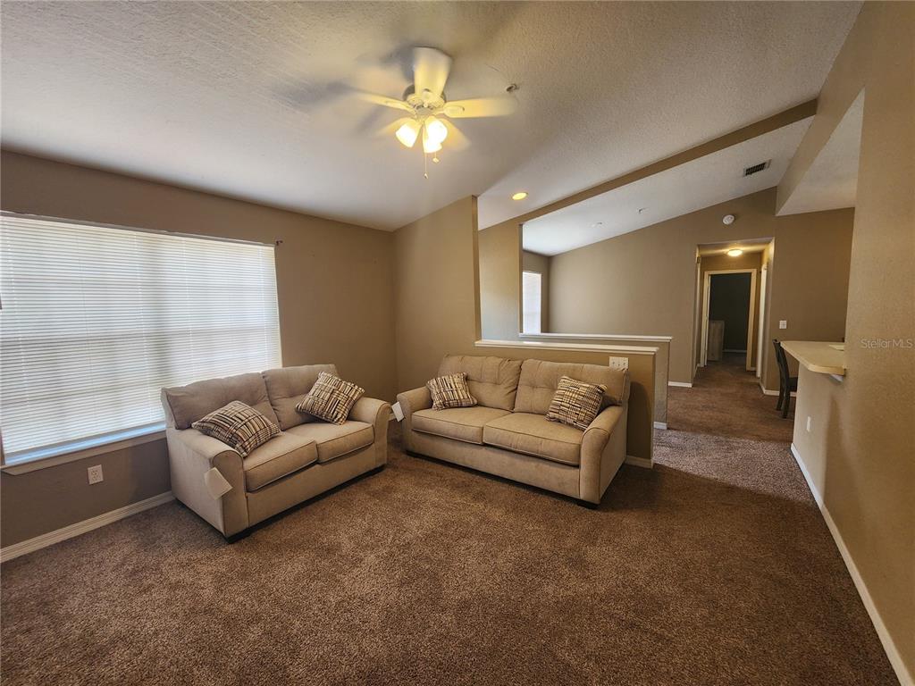 A living room features beige carpet, tan walls, two sofas, and a ceiling fan — 821 GRAND REGENCY POINTE UNIT 203, ALTAMONTE SPRINGS, FL