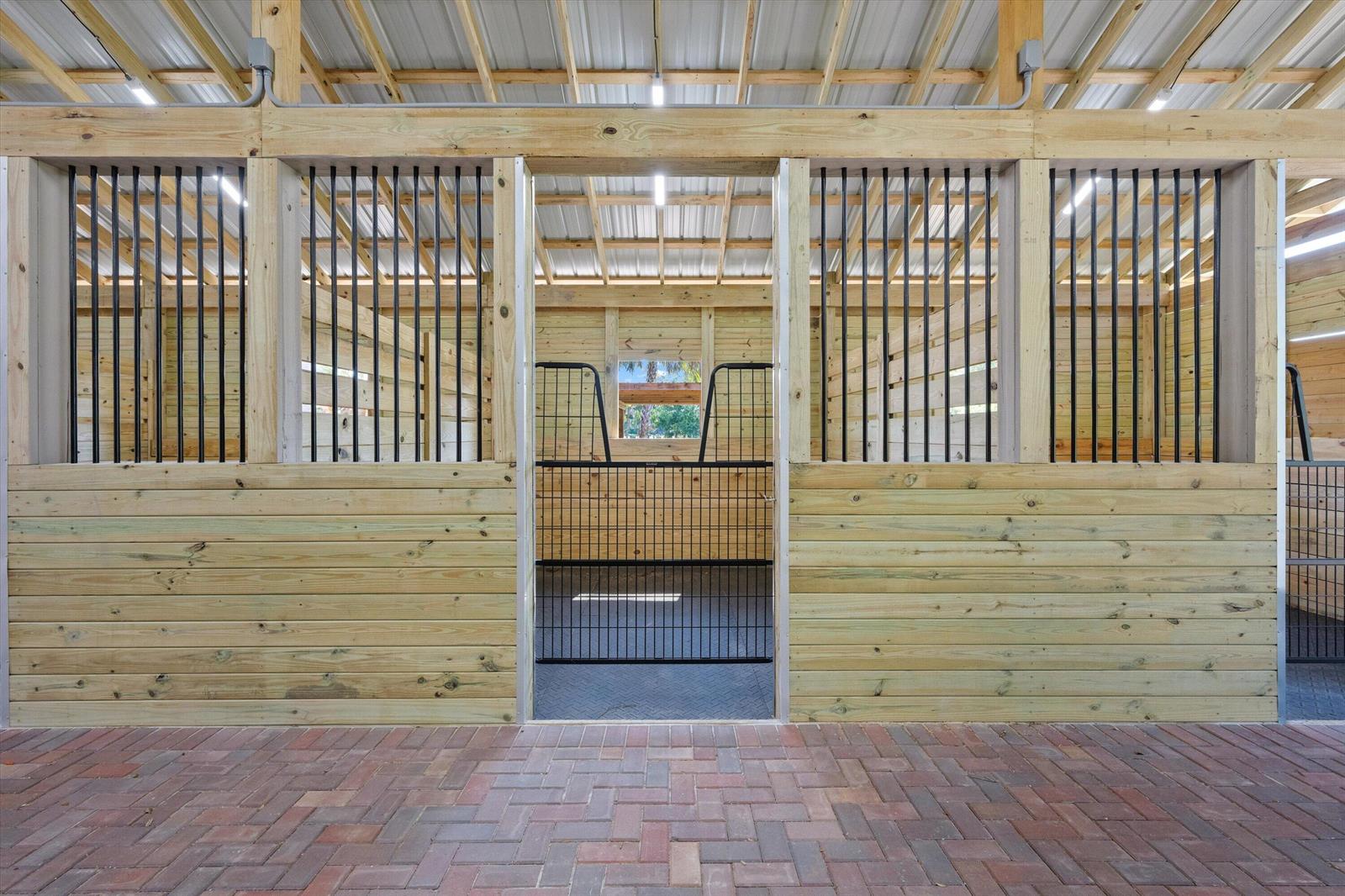 A horse stall with wooden walls, black metal bars, and a brick-paved aisle — 3509 C Road, FL 33470, FL