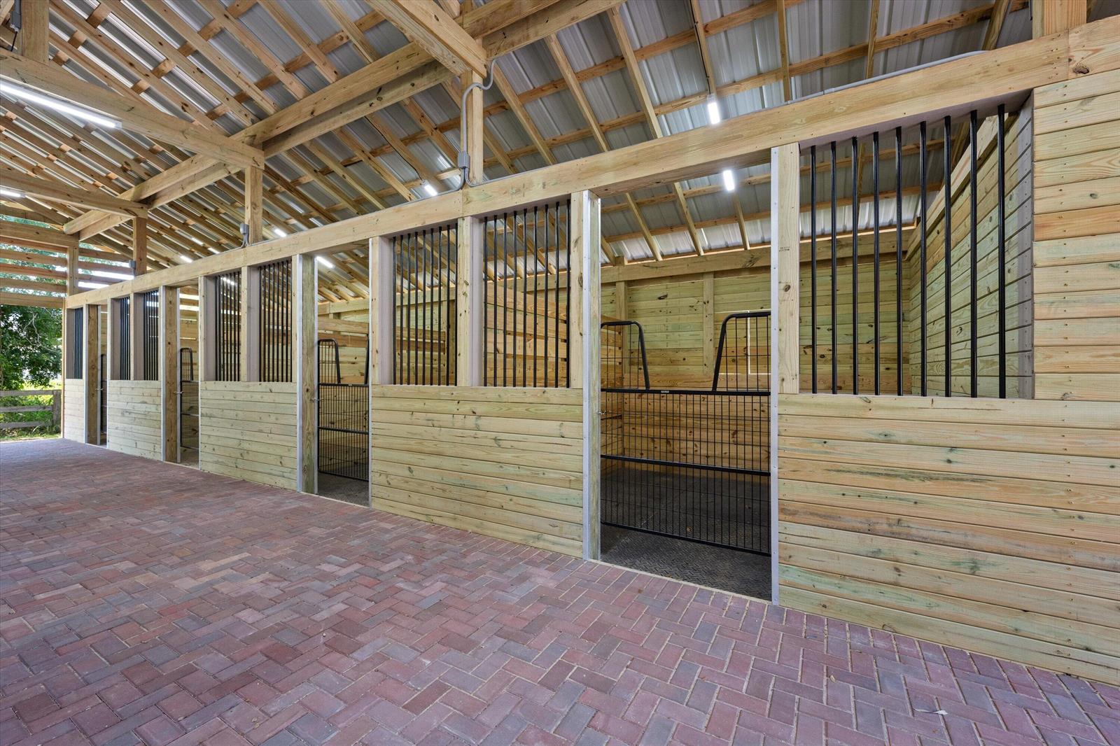 A row of horse stalls with wood walls, black metal grilles, and brick flooring — 3509 C Road, FL 33470, FL