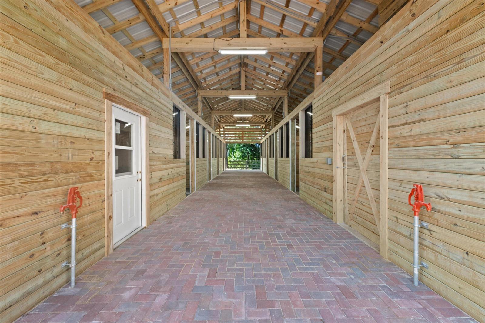 A barn interior features a brick-paved aisle flanked by wooden stalls and two water pumps — 3509 C Road, FL 33470, FL