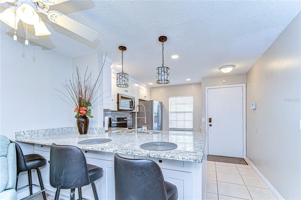 A kitchen with a granite-topped island, bar seating, white cabinets, and stainless steel appliances — 13870 OAKWOOD LANE UNIT 13870, SEMINOLE, FL