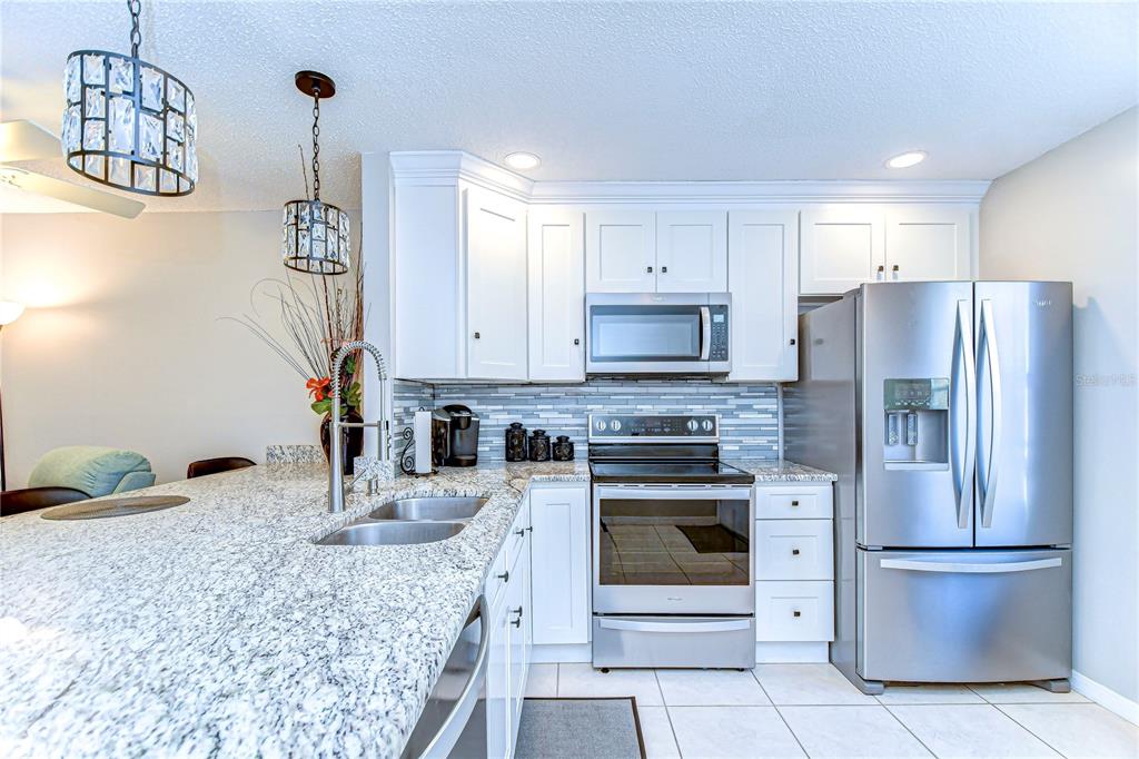A kitchen with white cabinets, granite countertops, stainless steel appliances, and a tiled backsplash — 13870 OAKWOOD LANE UNIT 13870, SEMINOLE, FL