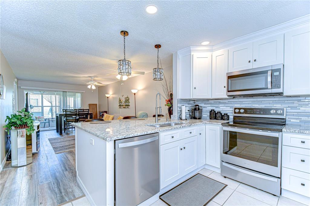 A kitchen with white cabinets, granite countertops, stainless steel appliances, and a view of the dining area — 13870 OAKWOOD LANE UNIT 13870, SEMINOLE, FL