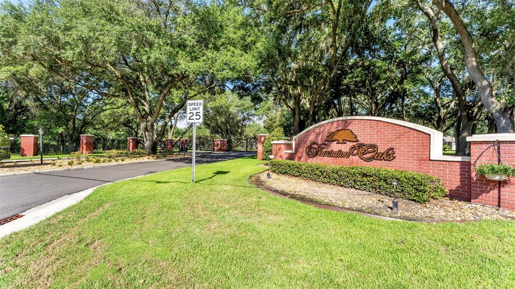 A brick entrance sign for Plantation Oaks stands beside a paved road under large trees — 6923 ORIANNA OAKS DRIVE, PLANT CITY, FL
