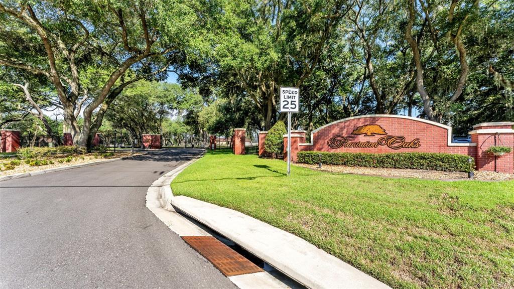 A brick entrance sign for Plantation Oaks stands beside a road under large oak trees — 6923 ORIANNA OAKS DRIVE, PLANT CITY, FL