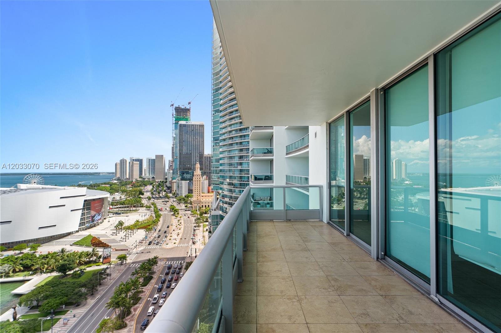 A high-rise balcony with tile flooring overlooks a city street, waterfront, and urban skyline — 900 Biscayne Blvd # 2304, Miami FL 33132, MIAMI, FL