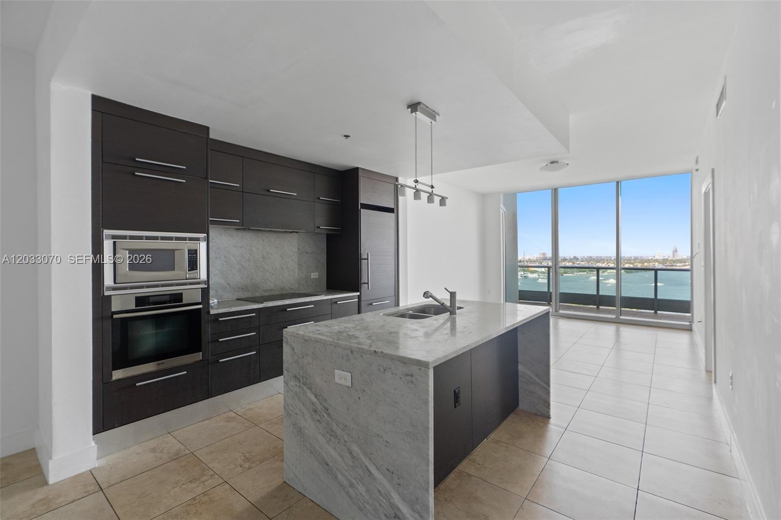 A modern kitchen features dark wood cabinetry, marble countertops, a central island, and floor-to-ceiling windows — 900 Biscayne Blvd # 2304, Miami FL 33132, MIAMI, FL