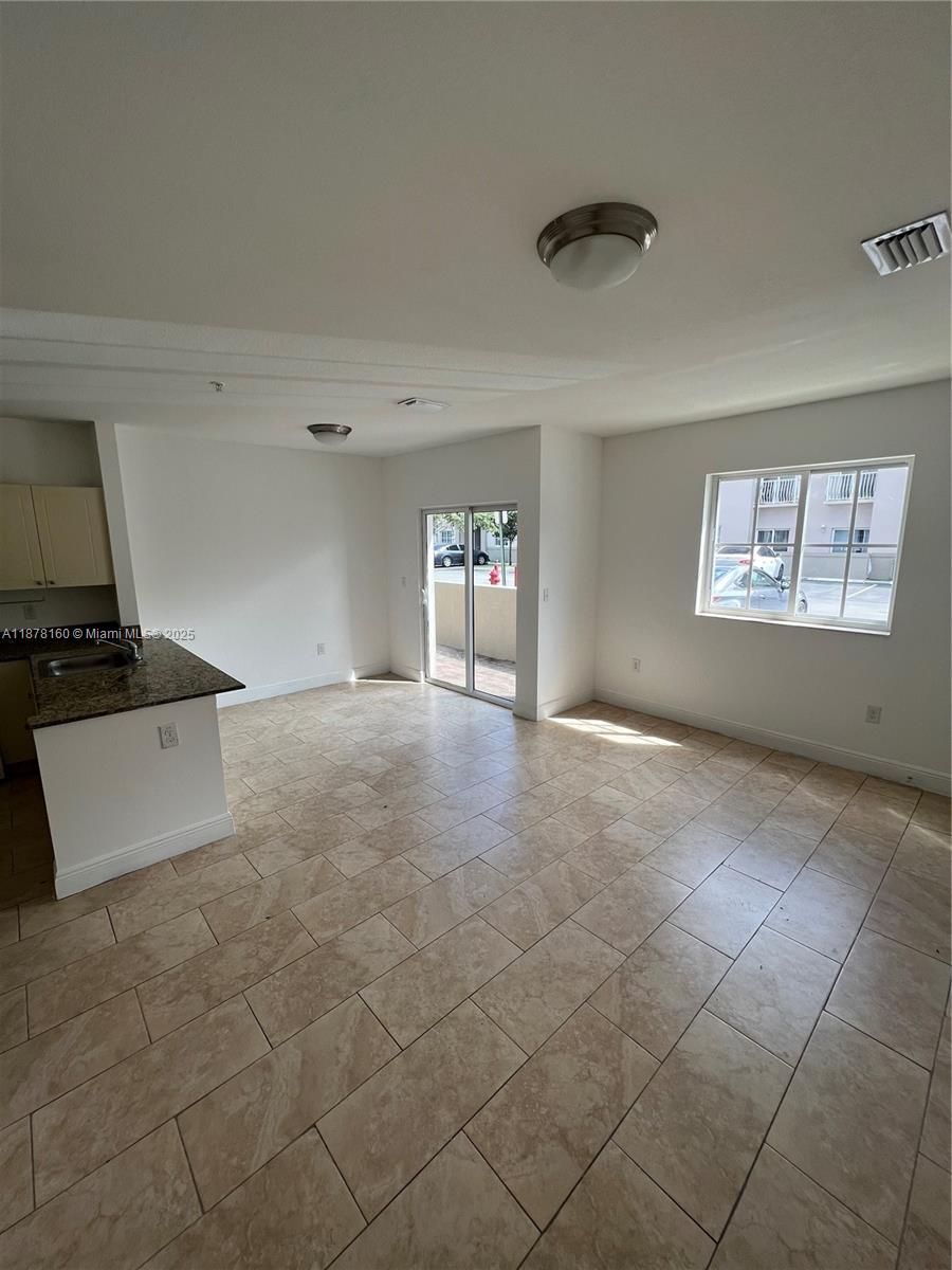 An open-concept kitchen and living area features tile flooring, a sliding glass door, and windows — 211 W 79th Pl # 302, Hialeah FL 33014, HIALEAH, FL