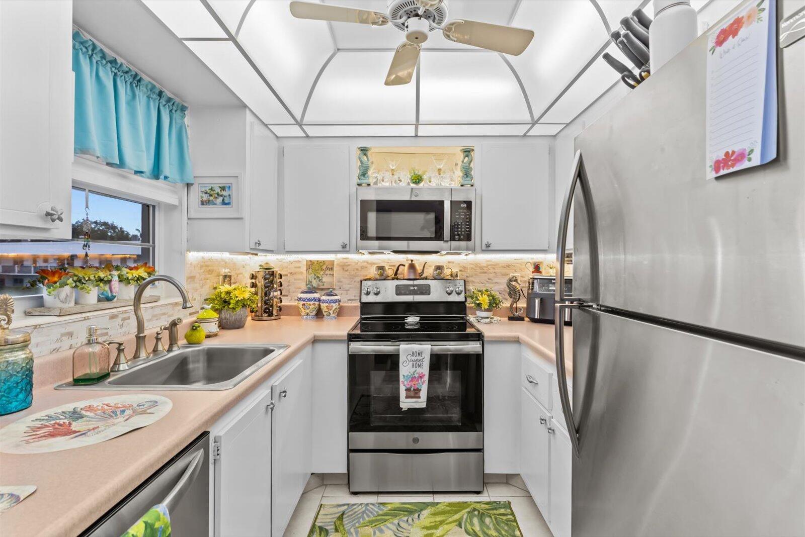 A galley kitchen features white cabinets, stainless steel appliances, a tiled backsplash, and a ceiling fan — 2929 SE Ocean Boulevard # 9, Stuart FL 34996, STUART, FL
