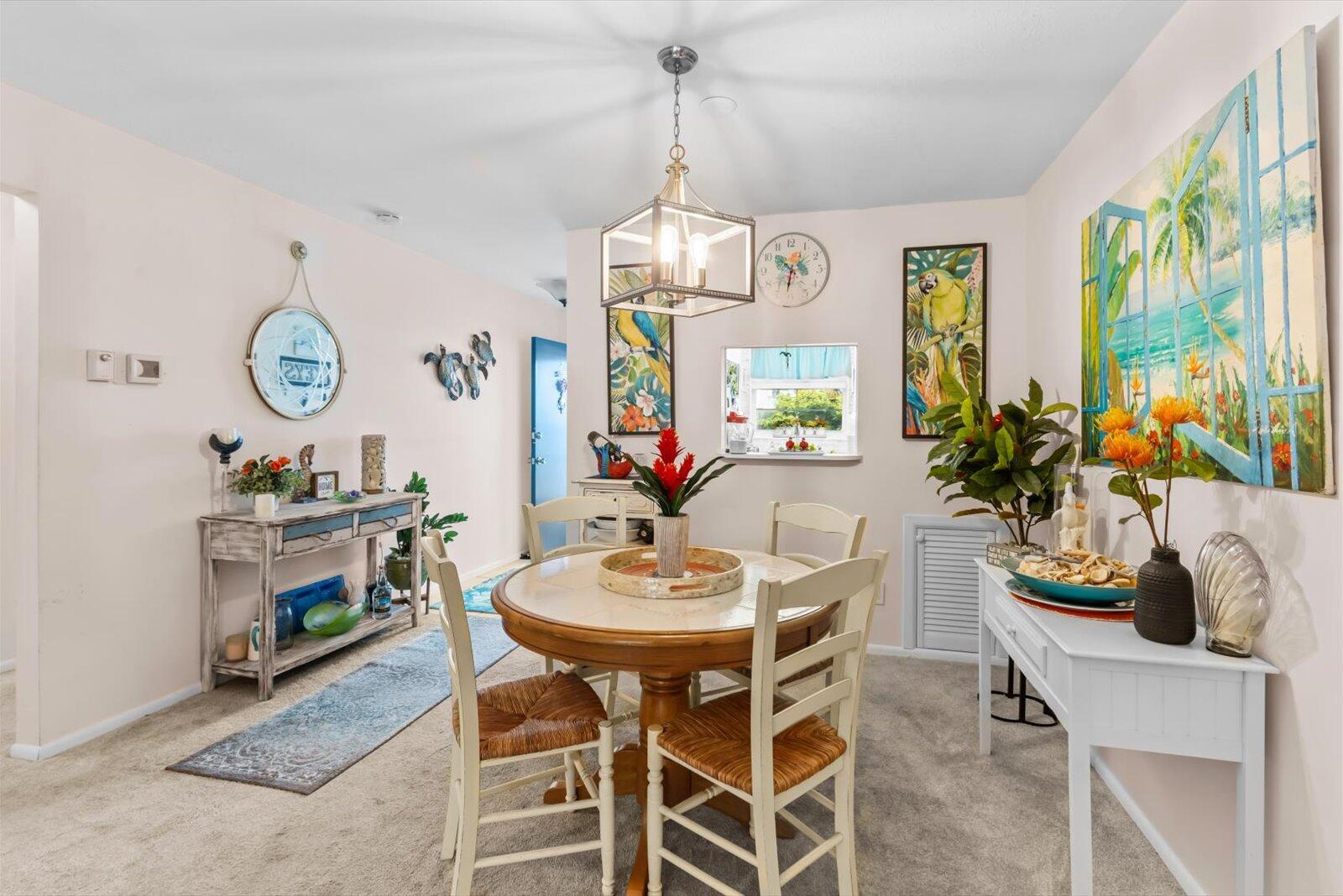 A dining room features a round wooden table, white chairs, and tropical-themed wall art — 2929 SE Ocean Boulevard # 9, Stuart FL 34996, STUART, FL