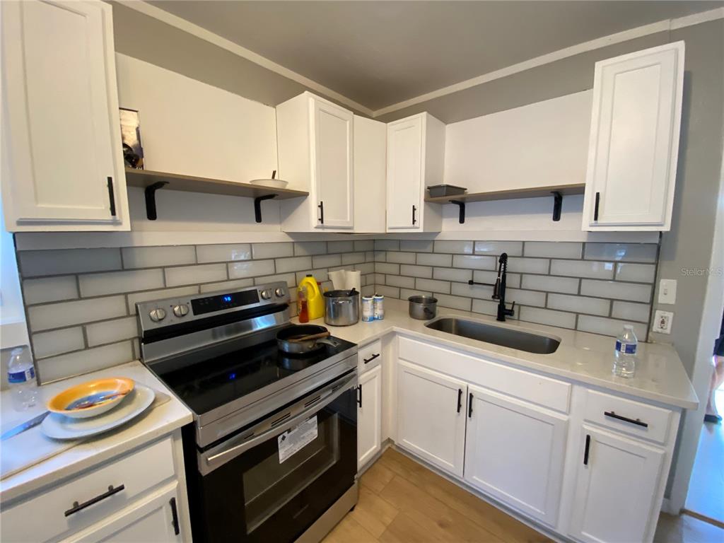 A kitchen features white cabinets, a stainless steel stove, a sink, and gray subway tile — 1847 19TH STREET S, ST PETERSBURG, FL