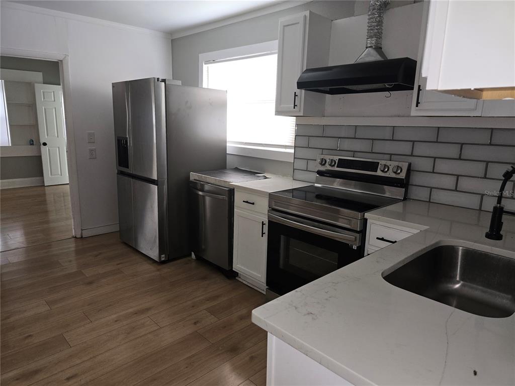 A kitchen features white cabinets, stainless steel appliances, a subway tile backsplash, and wood flooring — 1847 19TH STREET S, ST PETERSBURG, FL