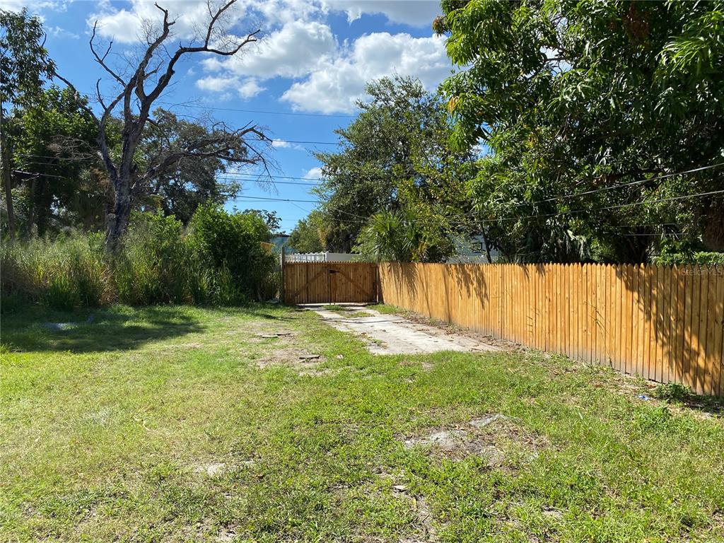 A grassy backyard features a wooden fence, a concrete driveway, and a gated entrance — 1847 19TH STREET S, ST PETERSBURG, FL