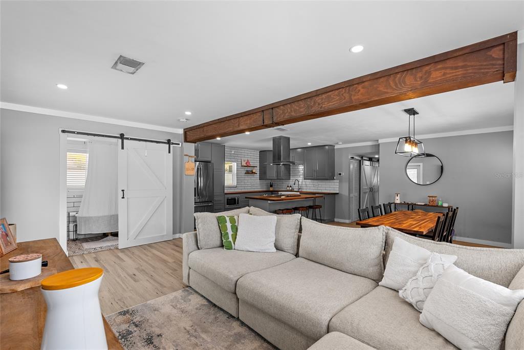 An open-concept living room and kitchen feature a wooden ceiling beam, gray cabinets, and flooring — 3412 W BAY AVENUE, TAMPA, FL