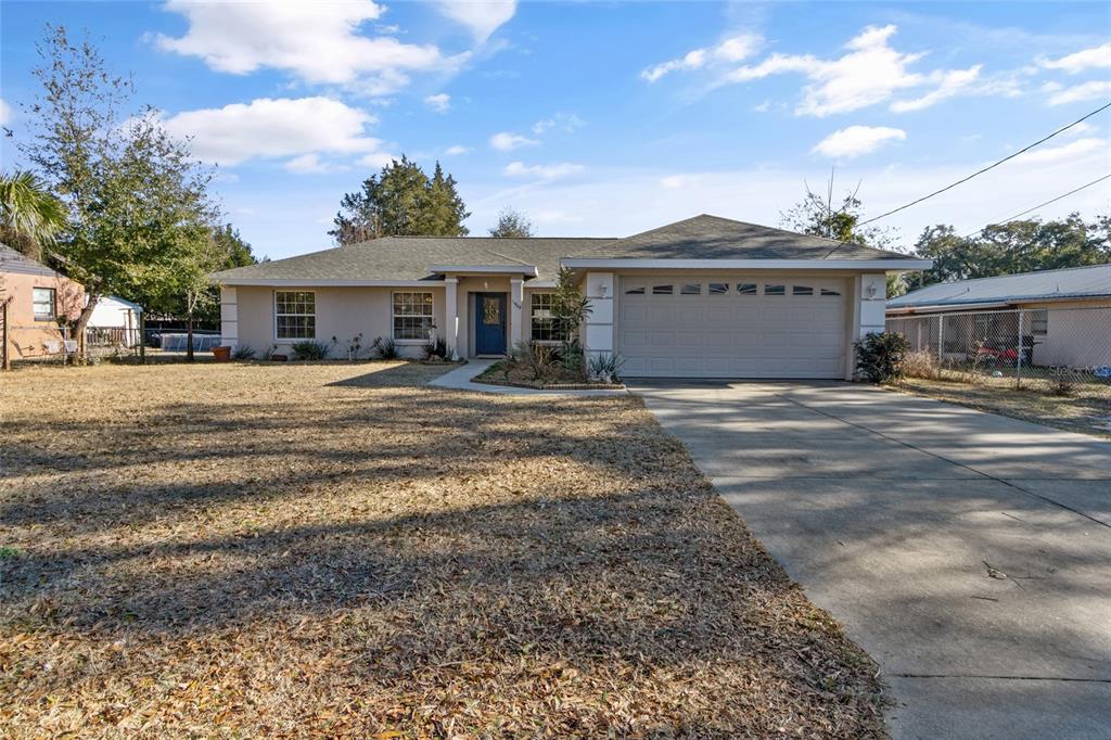 A single-story house with a beige exterior, a two-car garage, and a large front yard — 11965 SE 70TH AVENUE ROAD, BELLEVIEW, FL