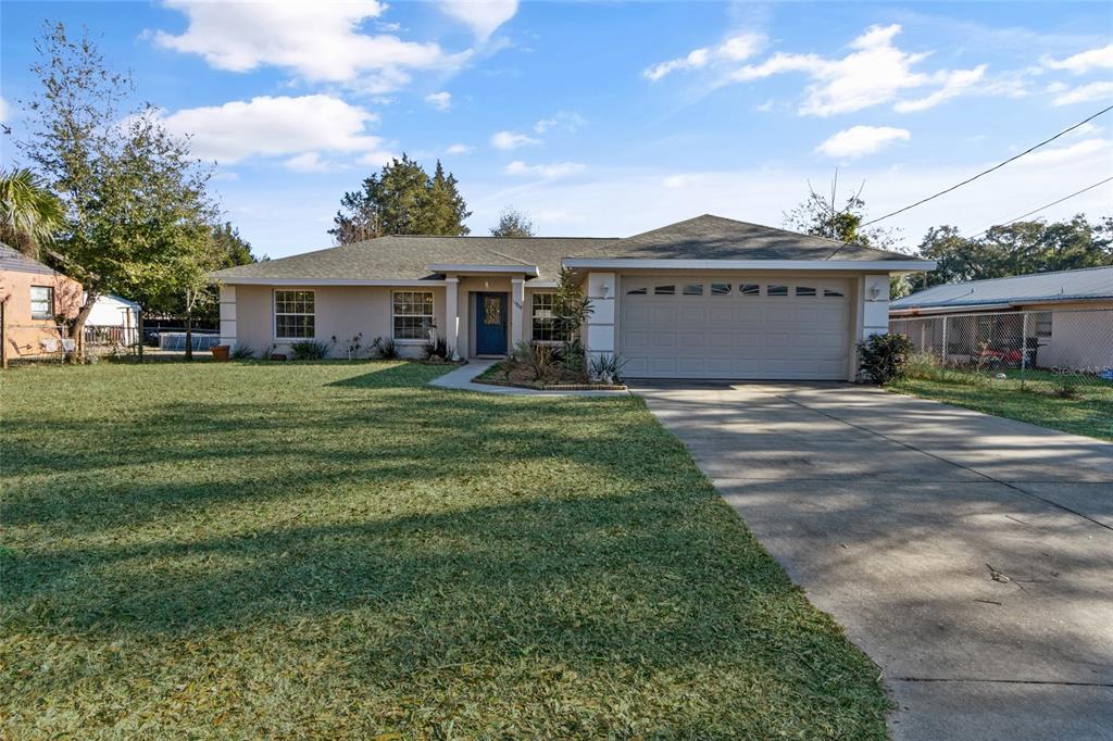 A single-story house with a beige exterior, a two-car garage, and a large front lawn — 11965 SE 70TH AVENUE ROAD, BELLEVIEW, FL