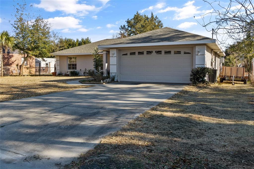 A single-story house with a beige stucco exterior, a two-car garage, and a concrete driveway — 11965 SE 70TH AVENUE ROAD, BELLEVIEW, FL