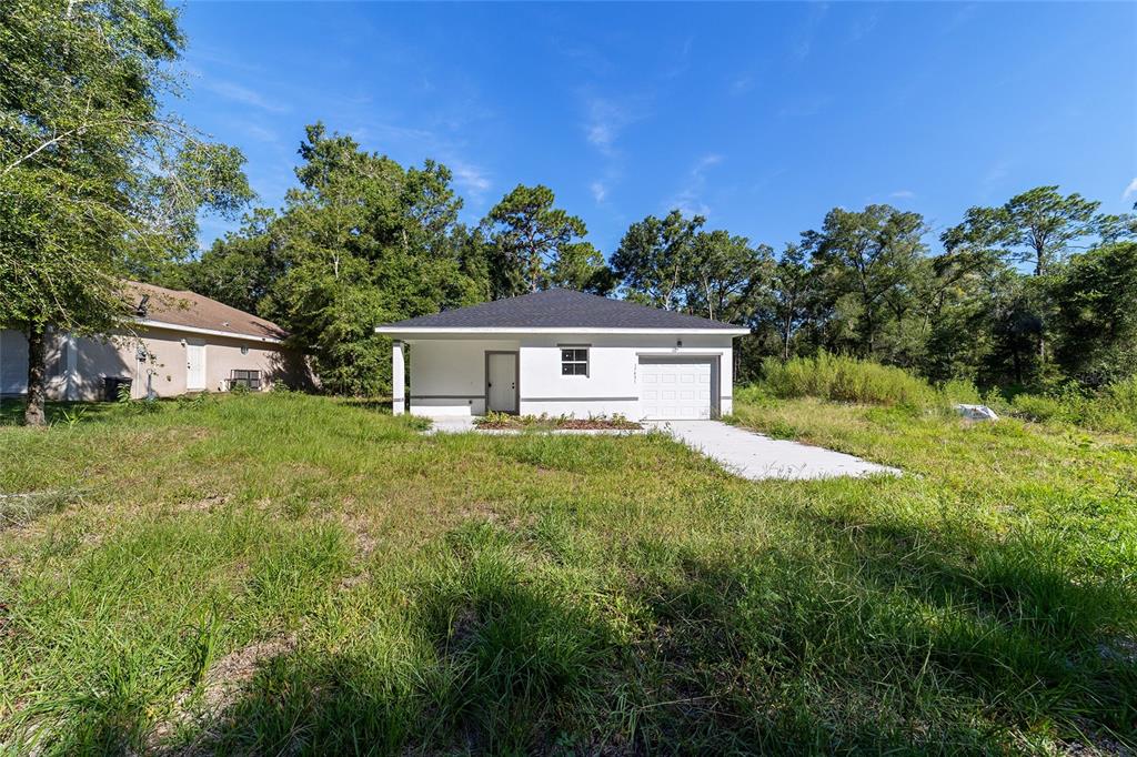 A white, single-story house with a dark roof and a one-car garage sits on grass — 15431 SOUTHWEST 41ST STREET ROAD, OCALA, FL
