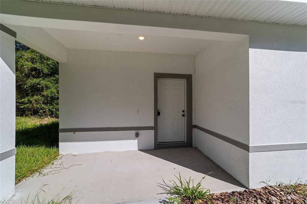 A covered concrete porch leads to a white front door with a gray frame — 15431 SOUTHWEST 41ST STREET ROAD, OCALA, FL