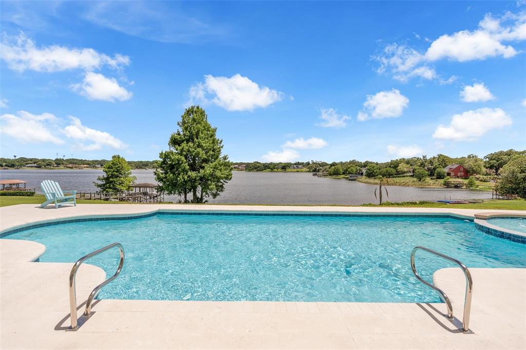 A swimming pool overlooks a lake with a blue sky and scattered clouds above — 9656 WEATHERSTONE COURT, WINDERMERE, FL